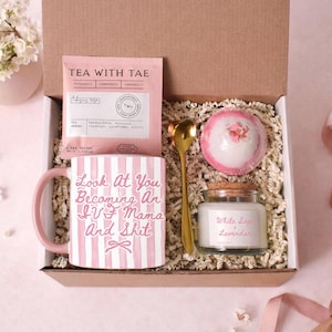 Könnte beinhalten: Geschenkbox mit einer rosa-weiß gestreiften Tasse mit der Aufschrift "Look At You Becoming An IVF Mama And Shit". Die Box enthält auch ein Teebeutel, eine Badekugel, eine Kerze und einen goldenen Löffel. Die Kerze ist mit "White Sage Lavender" beschriftet.