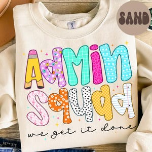 Op de afbeelding: Crèmekleurige sweatshirt met de woorden "Admin Squad" in kleurrijke, patroonletters. Het ontwerp bevat een potlood, sterren en de zin "we get it done" in zwart schrift. Een ronde "SAND"-afbeelding staat rechtsboven.