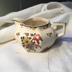 Pode incluir: Um cremoso de cerâmica branca com uma borda verde e um padrão floral. O cremoso tem uma forma octogonal e uma alça.