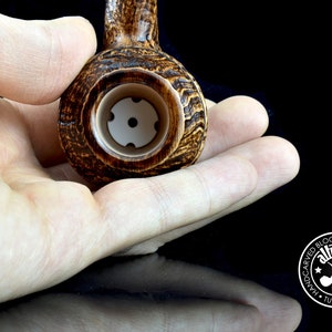 Puede incluir: Primer plano de una pipa de madera marrón con una cazoleta blanca. La pipa está siendo sostenida por una mano. La pipa está hecha por "Altinay Hand-Carved Block Meerschaum Pipes Turkey 1964".