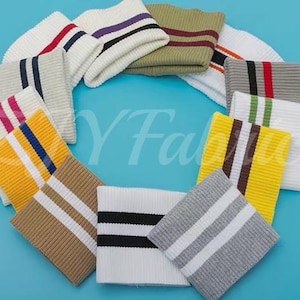 May include: A collection of ribbed knit fabric cuffs arranged in a circular pattern. Each cuff features a distinct color combination, including white, yellow, gray, tan, and olive, accented with two parallel stripes in contrasting colors like black, red, blue, or brown.