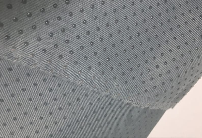Op de afbeelding: Close-up van een grijze stof met een subtiel textuurpatroon van kleine stippen. De stof heeft een licht glanzende afwerking.