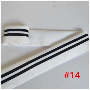 May include: Three white fabric bands with different colored stripes. The first band has two white stripes on a purple background. The second band has two black stripes on a white background. The third band has two gold glitter stripes on a white background. Each band is labeled with a number: #13, #14, and #15.