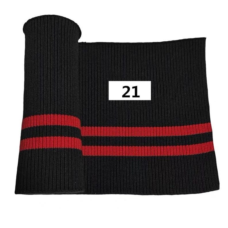 Puede incluir: Tejido de punto de canal&eacute; negro con dos rayas rojas. El tejido est&aacute; enrollado y el n&uacute;mero 21 est&aacute; impreso en una etiqueta blanca.