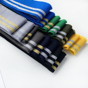 May include: Assortment of knit fabric trim with two stripes. The stripes are silver and gold. The fabric is in various colors including blue, gray, green, black, yellow, and khaki.