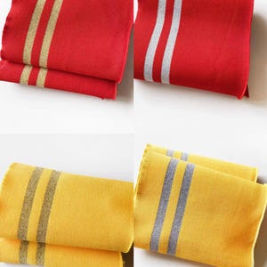 May include: Folded red and yellow cloth napkins with striped designs. The red napkins have gold and silver stripes, while the yellow napkins feature gray stripes. The napkins are neatly stacked, showcasing their texture and color variations.