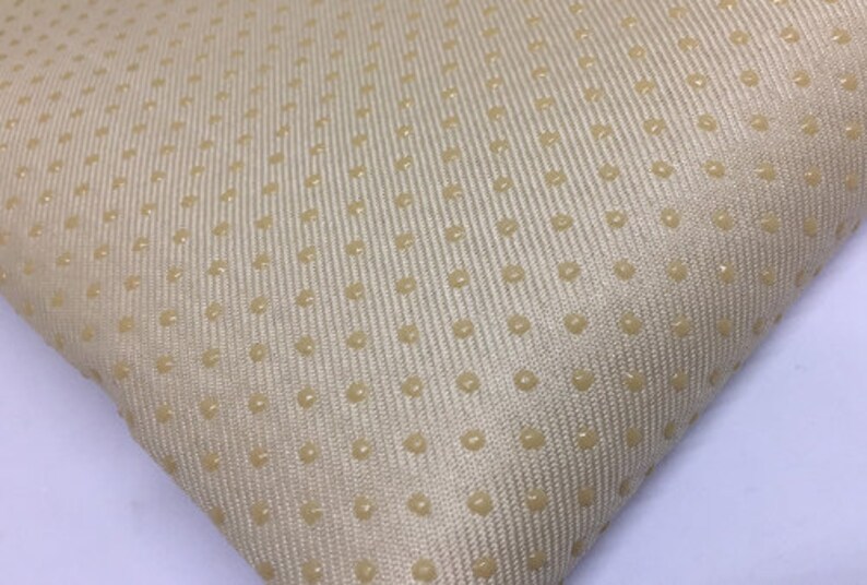 Op de afbeelding: Beige stof met een subtiel textuurpatroon van kleine, verhoogde stippen.