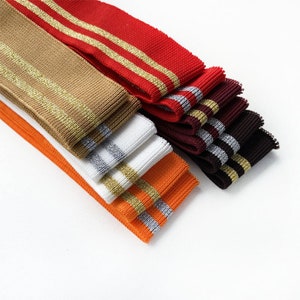 May include: A stack of different colored knit elastic trim with gold and silver stripes. The trim is folded and arranged in a fan shape.
