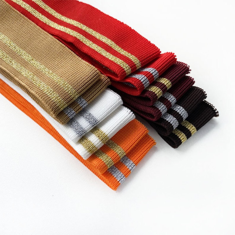 May include: A stack of different colored knit elastic trim with gold and silver stripes. The trim is folded and arranged in a fan shape.