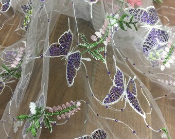 May include: White sheer fabric with embroidered purple butterflies and green leaves. The butterflies are decorated with iridescent sequins.