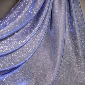 Könnte beinhalten: Nahaufnahme eines schimmernden blauen Stoffes mit glitzernder Textur. Der Stoff ist in weichen Falten drapiert, wodurch ein fließender Effekt entsteht. Das Material hat einen subtilen Glanz, der das Licht reflektiert und dem Design Tiefe verleiht. Der Gesamteffekt ist elegant und luxuriös.