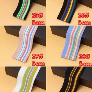 May include: Six different striped elastic bands in various colors, including black, white, green, pink, blue, and yellow. The bands are 5 cm wide and are labeled with numbers 25 through 30.