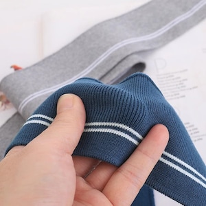May include: Close-up of a blue fabric with white stripes. The fabric is ribbed and has a soft texture.