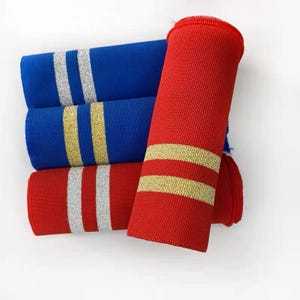 May include: Close-up of three rolled fabric tubes in red and blue. The blue tubes have silver stripes, while the red tubes have gold stripes. The fabric appears to be a knit material.
