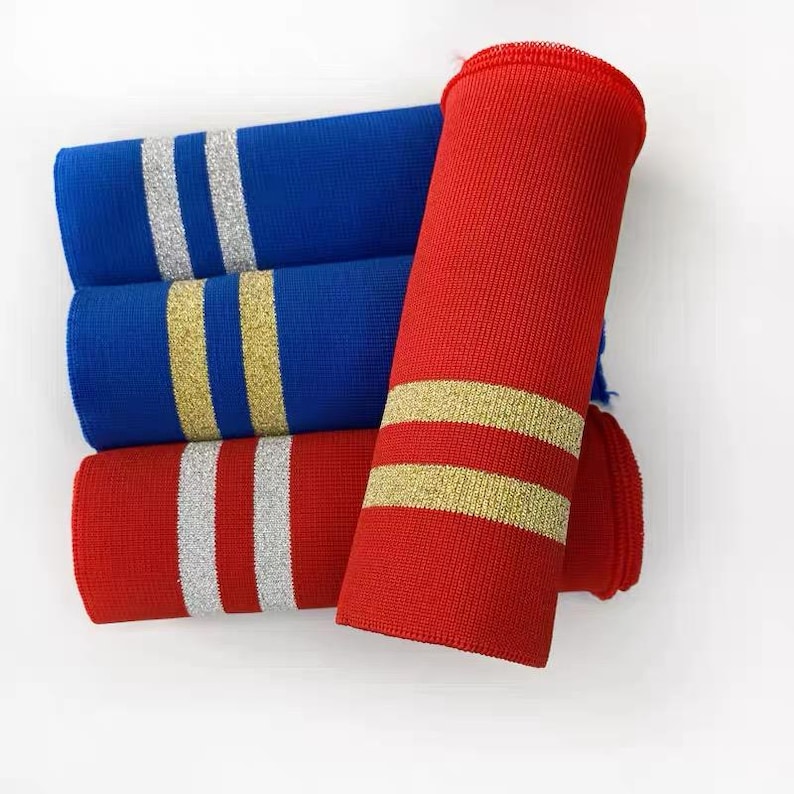 May include: Close-up of three rolled fabric tubes in red and blue. The blue tubes have silver stripes, while the red tubes have gold stripes. The fabric appears to be a knit material.