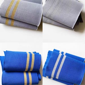 May include: Four folded fabric pieces in the image. Two are gray with gold stripes, and two are blue with gold stripes. The other two blue pieces have silver stripes. The fabric has a textured appearance.