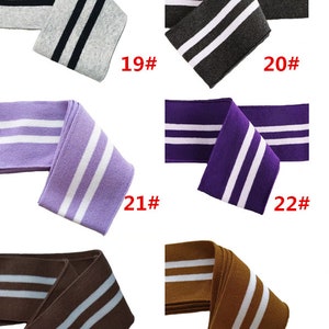 Op de afbeelding: Zes verschillende kleuren gebreide stof met twee witte strepen. De kleuren zijn grijs, donkergrijs, paars, lichtpaars, bruin en beige. De stof is gemarkeerd met de nummers 19, 20, 21, 22, 23 en 24.