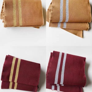 May include: Four folded rectangular scarves. Two are tan with gold stripes, and two are tan with silver stripes. The other two are burgundy with gold stripes, and burgundy with silver stripes. All have a textured weave.