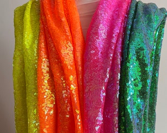 Puede incluir: Cuatro telas de lentejuelas iridiscentes de diferentes colores, mostradas en un maniquí blanco. Los colores son verde lima, naranja, rosa y azul verdoso.