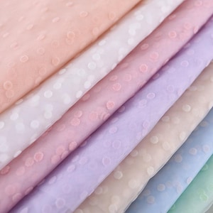 May include: A close-up of several layers of sheer fabric in pastel colors, including pink, white, lavender, and blue. The fabric has a delicate polka dot pattern, creating a soft and airy texture. Ideal for crafting and sewing projects.