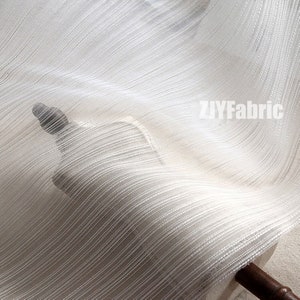 May include: White sheer fabric with a subtle striped pattern. The fabric is draped over a wooden dowel.