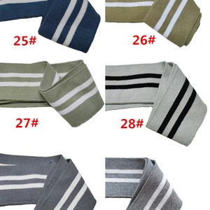 Op de afbeelding: Vijf verschillende kleuren gebreid stof met twee witte strepen. De stof is gevouwen en gelabeld met de nummers 25, 26, 27, 28, 29 en 30.
