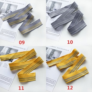 May include: Four samples of elastic trim with silver glitter stripes. The trim is available in gray, yellow, and two shades of yellow. The trim is labeled with numbers 09, 10, 11, and 12.