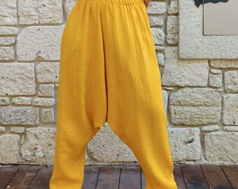 May include: A woman wearing a green velvet strapless top and mustard yellow, loose-fitting pants. She is standing in front of a stone wall.