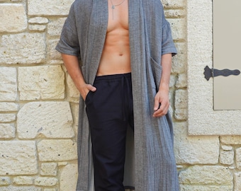 May include: A gray, long-sleeved robe with a shawl collar and a relaxed fit. The robe is made of a soft, lightweight fabric and has a subtle texture. The model is wearing black pants and is barefoot.