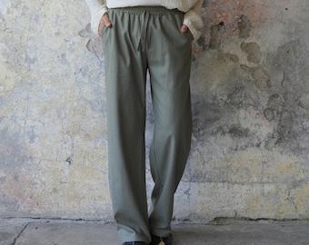 May include: A cream-colored, long-sleeved V-neck shirt and olive green drawstring pants. The shirt has a textured appearance, and the pants have a relaxed fit. The outfit is casual and comfortable, suitable for everyday wear.