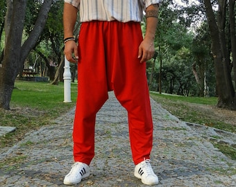 May include: A person wearing a striped blue and white long-sleeved shirt and red pants with a loose fit. The person is standing on a paved path in a park.