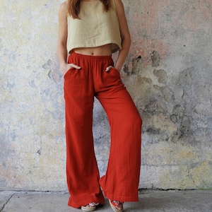 Könnte beinhalten: Eine Frau trägt ein hellbraunes, ärmelloses Crop-Top und eine rote, weitbeinige Hose. Die Hose hat eine weite Beinweite und eine hohe Taille.