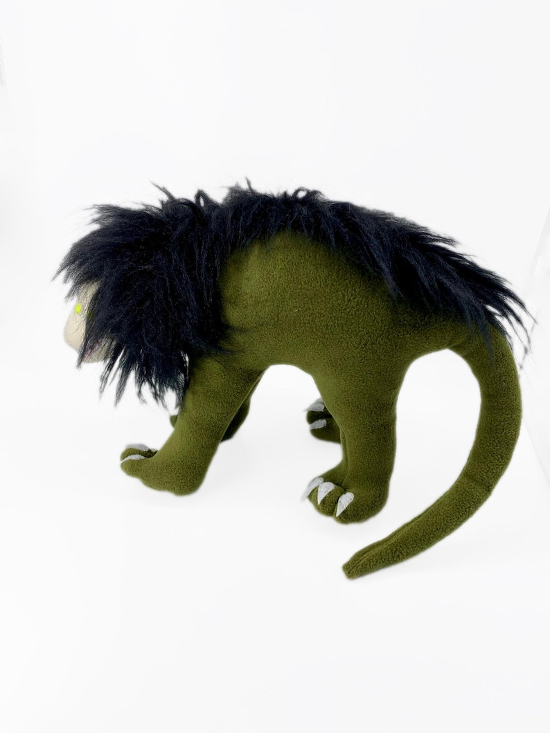 May include: Green plush toy with black fur and a long tail. The toy has a green body with a long tail and black fur on its head. The toy has a green body with a long tail and black fur on its head.