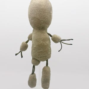 Puede incluir: Un juguete de peluche beige con una cabeza redonda y extremidades largas. El juguete tiene una cuerda atada a cada extremidad y una cuerda atada a la cabeza.
