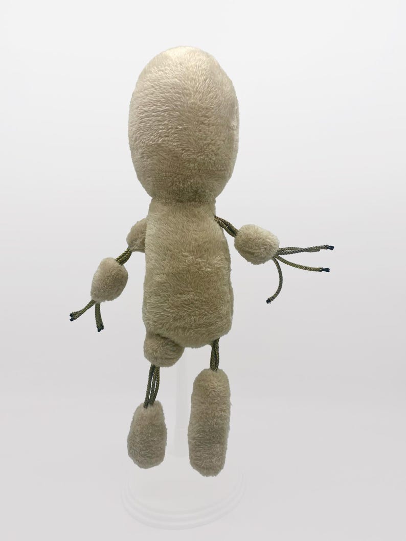 Puede incluir: Un juguete de peluche beige con una cabeza redonda y extremidades largas. El juguete tiene una cuerda atada a cada extremidad y una cuerda atada a la cabeza.