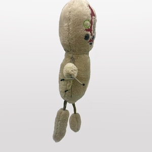 Puede incluir: Un juguete de peluche de una figura humanoide con una cara roja y blanca, ojos verdes y pelaje marr&oacute;n. El juguete tiene cuatro extremidades y est&aacute; de pie sobre un fondo blanco.