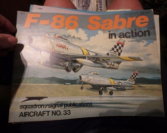 May include: A book cover featuring a detailed illustration of two silver F-86 Sabre fighter jets in flight. The book title is "F-86 Sabre in action" and the subtitle is "squadron/signal publications AIRCRAFT NO. 33".