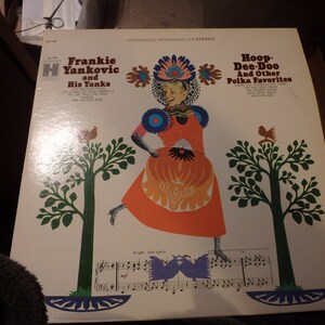 May include: A vintage vinyl record album cover featuring Frankie Yankovic and His Yanks. The cover art depicts a woman in a colorful folk costume dancing with a bright orange skirt and a red bodice. The album title is "Hoop Dee-Doo and Other Polka Favorites".