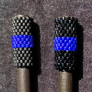 May include: Two black and blue beaded pen toppers with a thin blue stripe. The pen toppers are made of small black beads and a single blue stripe of beads.