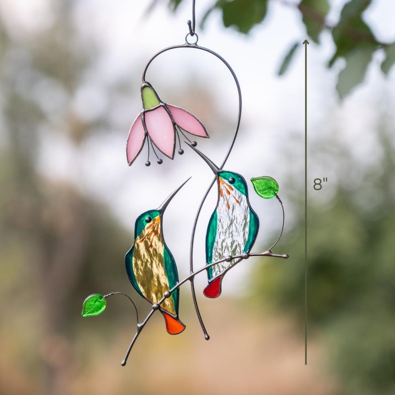 Two stained glass hummingbirds with a pink flower stained glass ornament as a window decor