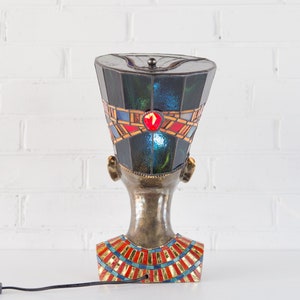 May include: A stained glass lamp shaped like an Egyptian queen's head with a blue, green, red, and gold design.