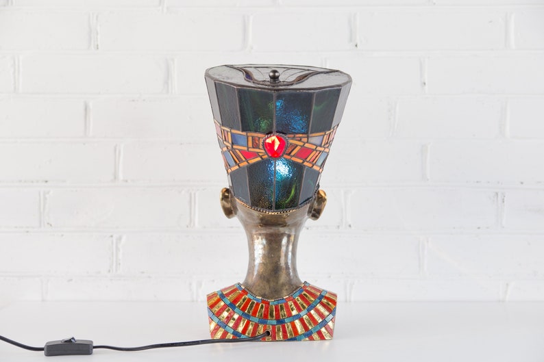 May include: A stained glass lamp shaped like an Egyptian queen's head with a blue, green, red, and gold design.