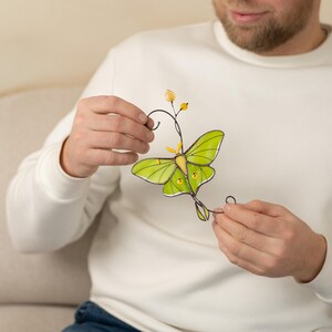 A man carefully presenting the Luna Moth window hanging. The light catches the yellow accents on the wings, illustrating how the art piece brightens up indoor and outdoor spaces.
