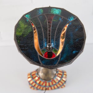May include: A stained glass lamp with a blue, green, and red design. The lamp base is a sculpted bust with a gold and red patterned collar.