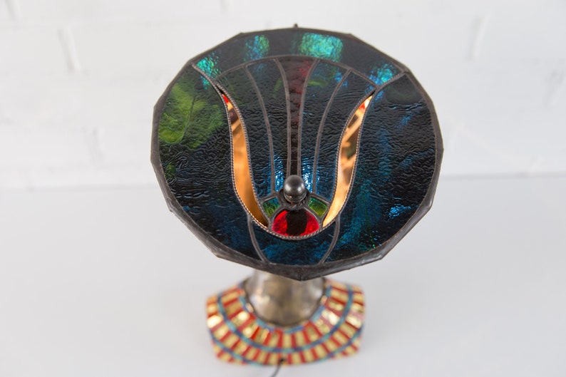 May include: A stained glass lamp with a blue, green, and red design. The lamp base is a sculpted bust with a gold and red patterned collar.