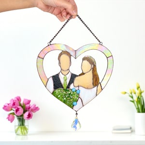 Heart-shaped stained glass wedding portrait being held above a white table decorated with pink and yellow flowers.