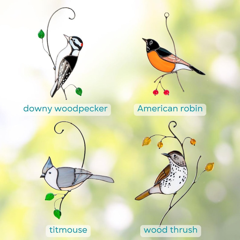 Collection of handmade stained glass bird suncatchers featuring a downy woodpecker, American robin, titmouse, and wood thrush, displayed on decorative wire branches against a soft green blurred background.