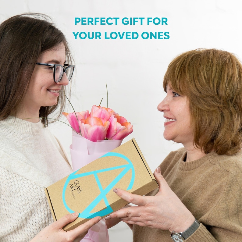 A smiling woman hands a Glass Art Stories gift box to her mother, holding a bouquet of tulips, with the caption “Perfect gift for your loved ones”