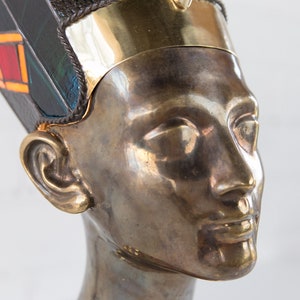 May include: A bronze bust of an Egyptian queen wearing a gold and blue headdress with intricate details.