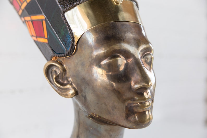 May include: A bronze bust of an Egyptian queen wearing a gold and blue headdress with intricate details.
